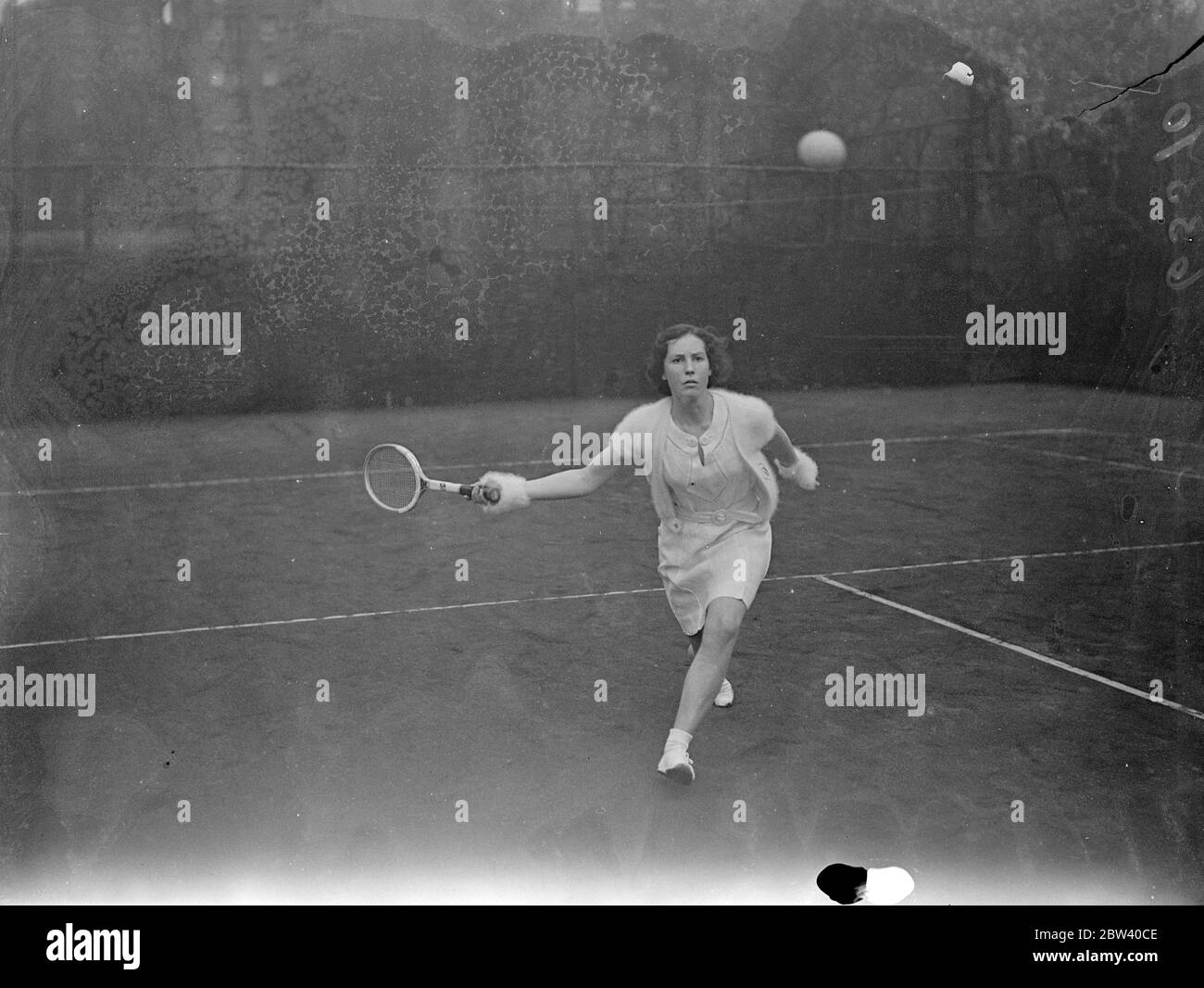 Girl in mittens at Melbury clubs tennis tournament . Leading tennis players , men and women , are turning out for Wimbledon in the Melbury clubs tournament at Kensington . This tournament is the first tryout of real lawn tennis strength this season . Photo shows , Miss H Dundas wearing white fleecy mittens in her match against Miss J Harvest . 12 April 1937 Stock Photo