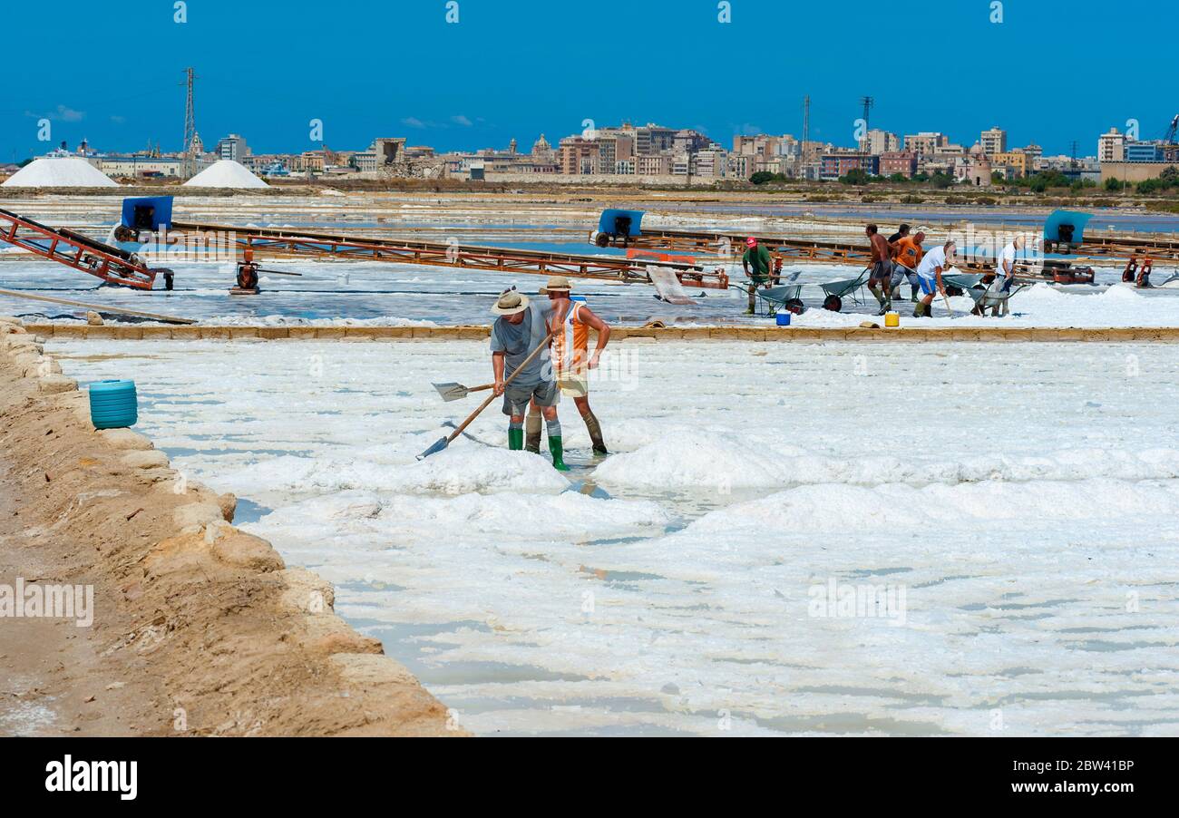 Trapani, August 13, 2016 - Italy: Workers shoveled the salt crystallizes out of the ground in salt farm , filled with natural salt from the sea. Stock Photo
