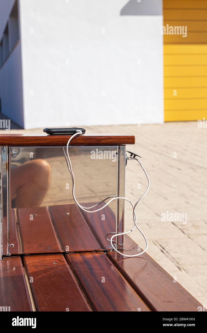 Solar powered USB charger with mobile phone on charge and bench outside on the footpath in Playa San Juan, tenerife, Canary Islands, Spain Stock Photo