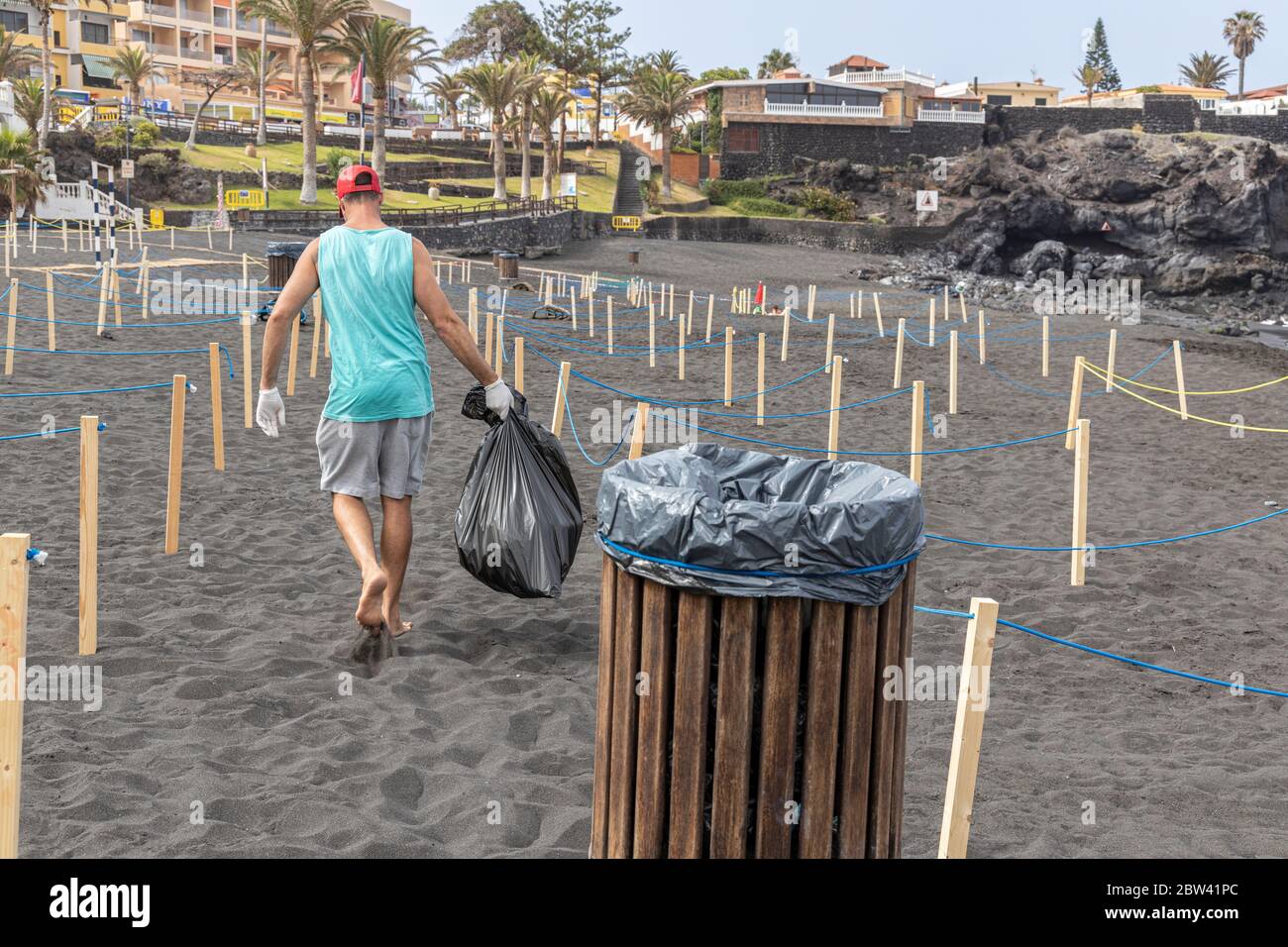 Worker empties rubbish bin on the beach with cordoned off areas to maintain social distancing, two metres apart, and controlled access for the public Stock Photo