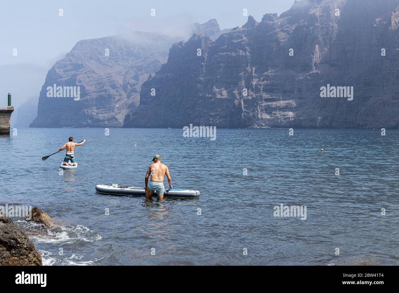 Two young men go out on SUP, stand up paddle boards from the beach during phase two de-escalation of the Covid 19, coronavirus state of emergency.  Pl Stock Photo