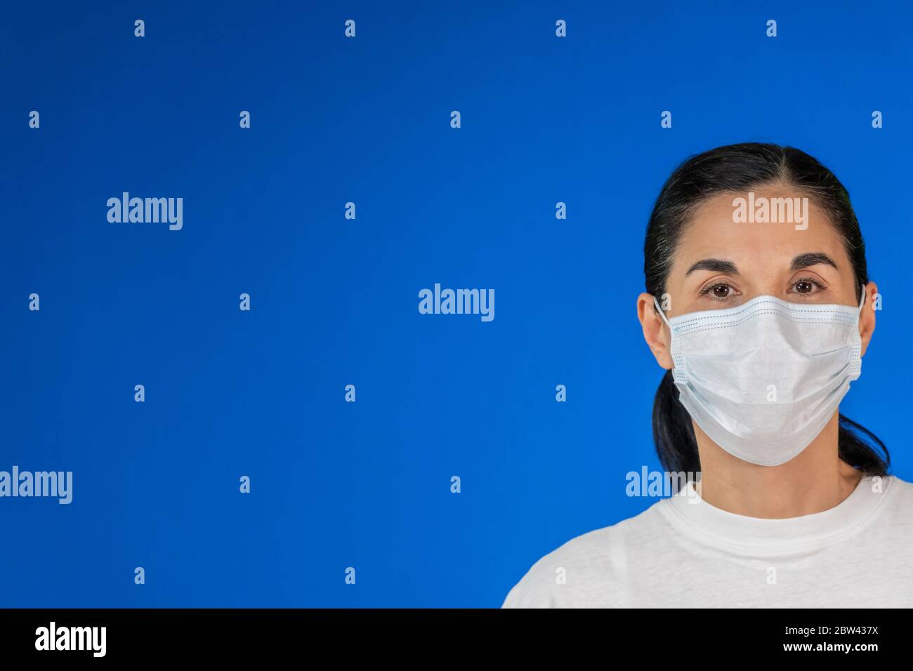 Isolated Woman wearing protective mask against blue background and with large copy space. Health issue concept, preventive measure against Covid-19 Stock Photo