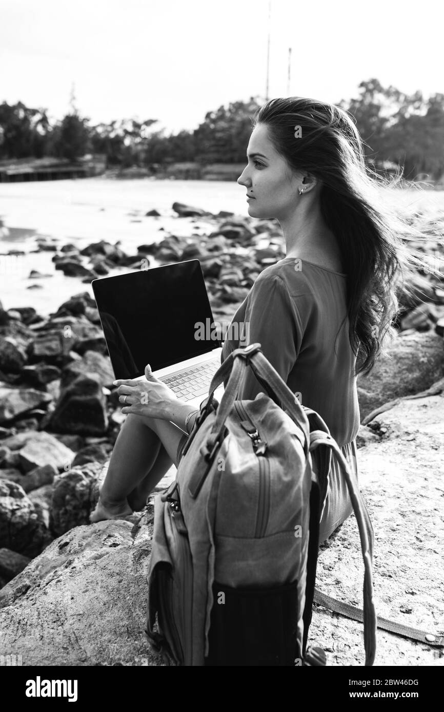 Young female freelancer working on a laptop while traveling by the sea, remote work concept. Using modern technology, the Internet for communication. Stock Photo