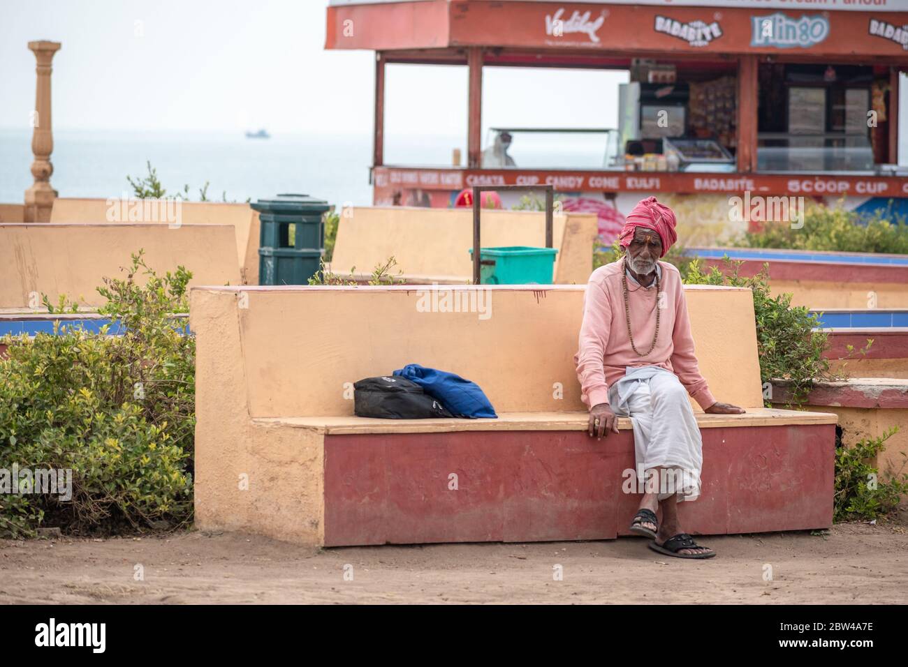 Somnath, Gujarat, India - December 2018: An elderly Indian man sitting on  a bench in a seaside park in the town of Somnath. Stock Photo