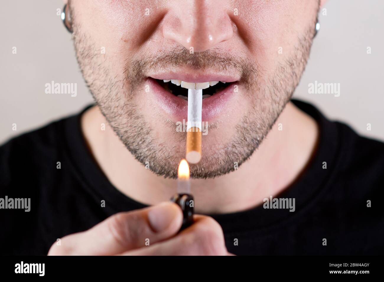 an unshaven handsome man is about to light a cigarette with a lighter
