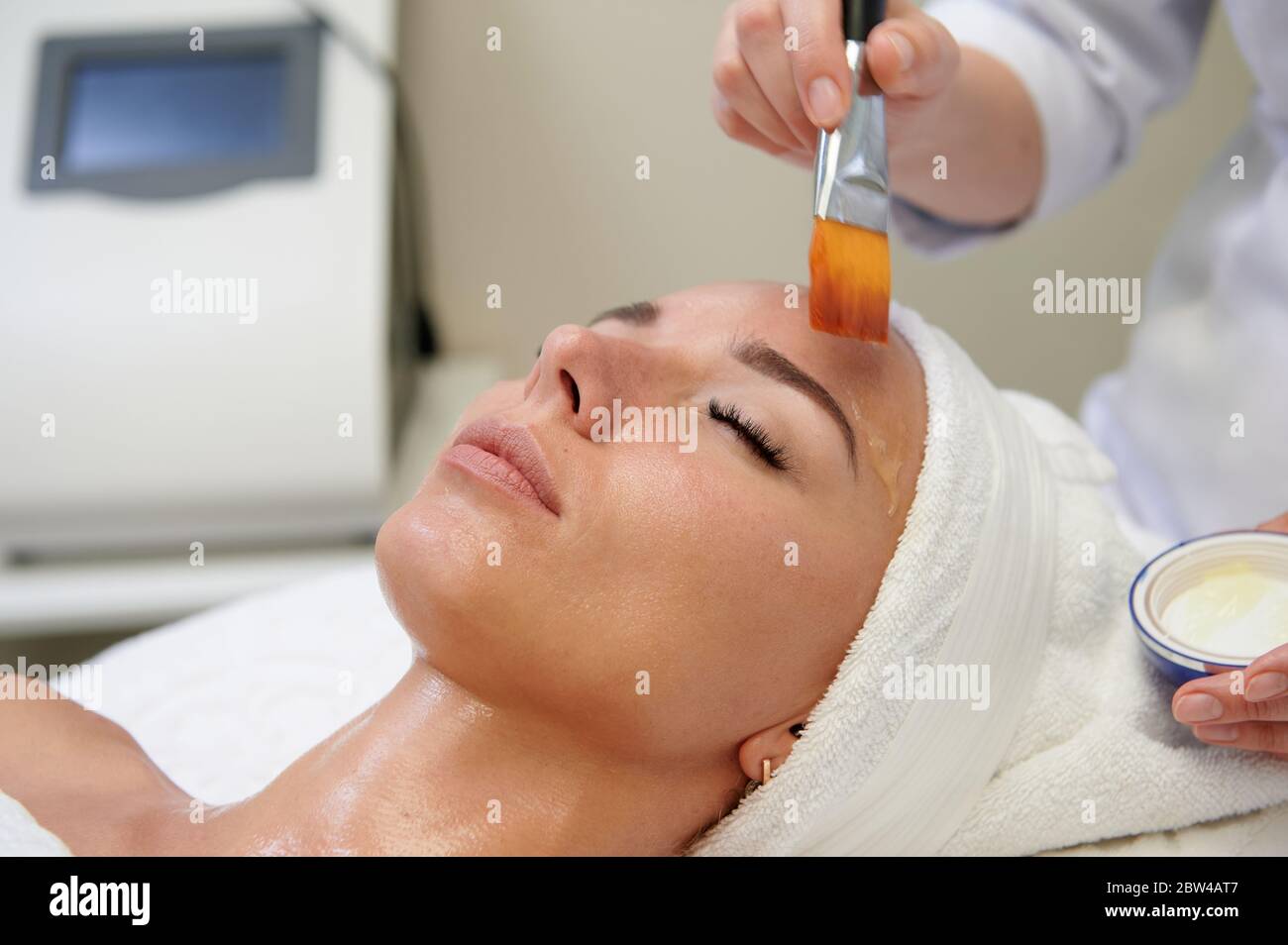 Applying facial mask with orange brush in spa treatment alternative medicine Stock Photo