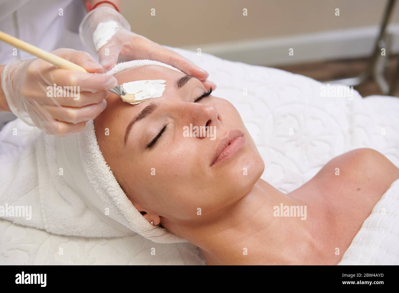 Applying white facial mask with brush in spa treatment alternative medicine Stock Photo