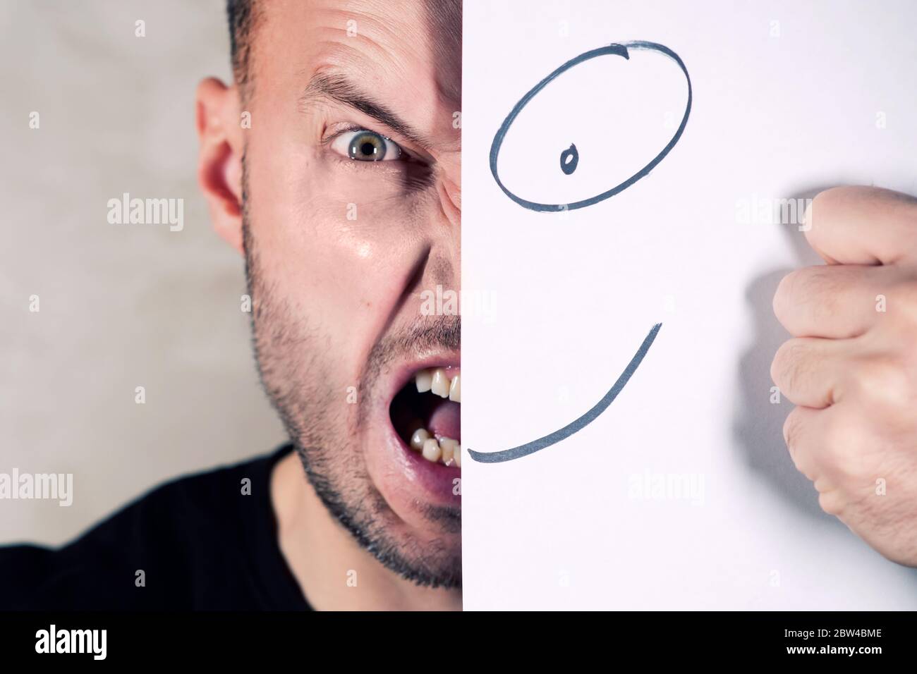 screaming man covers half face with painted smile, close up Stock Photo
