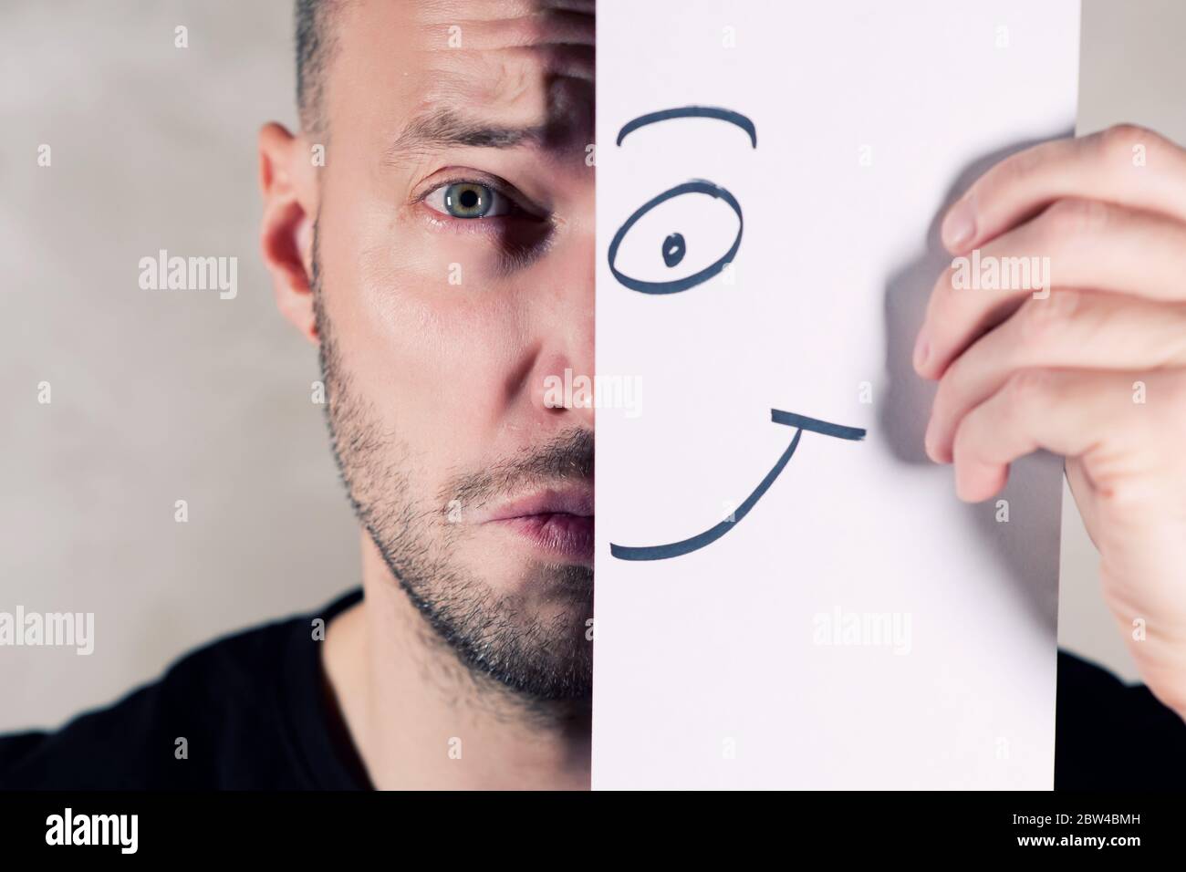 a smile painted on paper partially covers the face of a sad man, close up Stock Photo