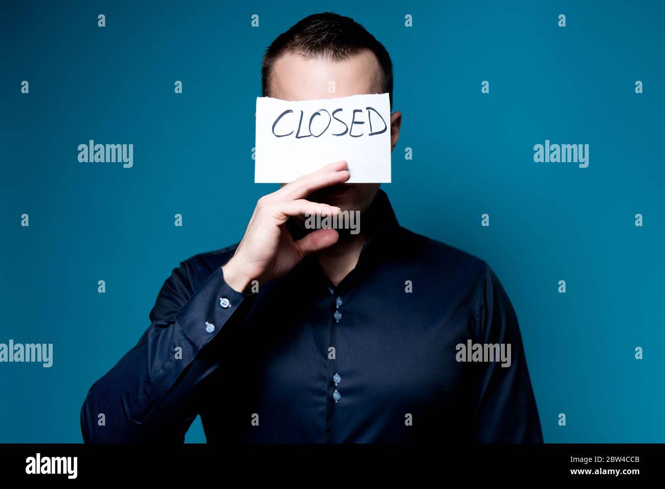 a man in a blue shirt covers his face with a sign saying closed Stock Photo