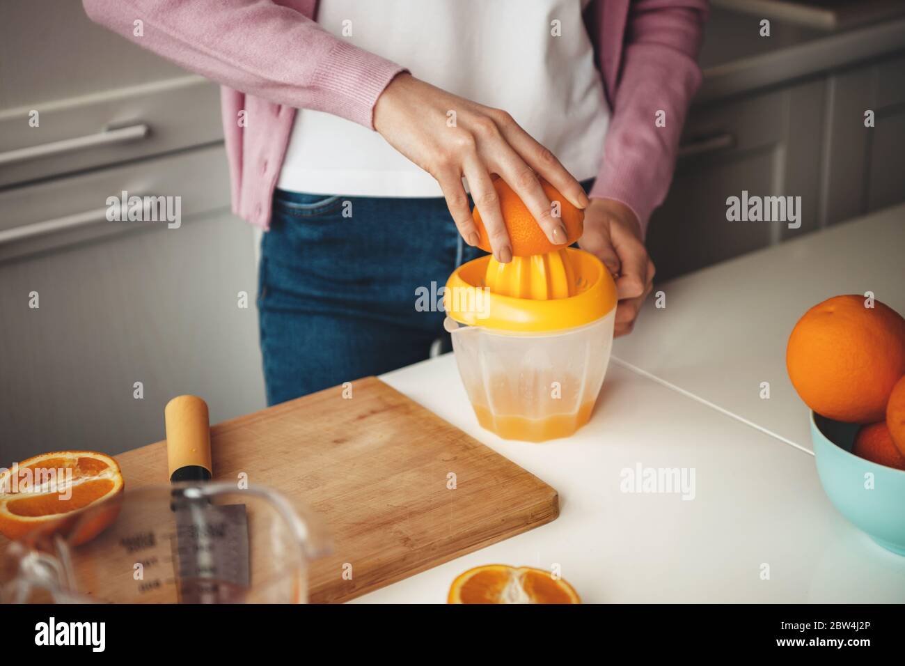 Close up photo of a caucasian lady making juice from orange on the table using a squeezer Stock Photo