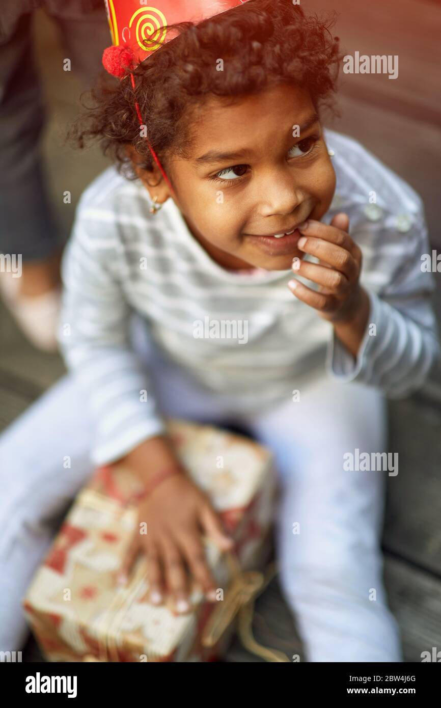 Little cute afro-americangirl in birthday cap holding  birthday presents. Stock Photo