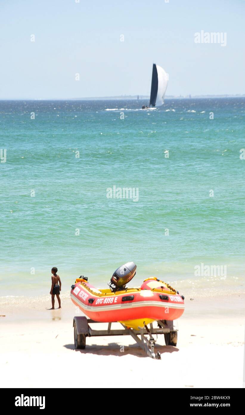 A scene at Cottisloe beach, Western Australia. In the distance is a yacht flying a spinnaker sail and in foreground there is ai inflatable boat with o Stock Photo