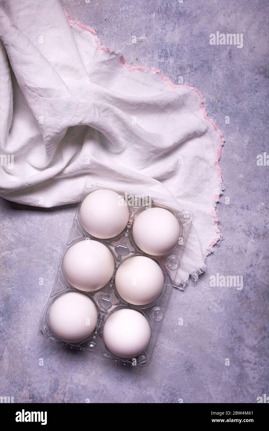 on the gray textured background, with a top view, a cotton tea towel and half a dozen white eggs for the preparation of culinary recipes Stock Photo