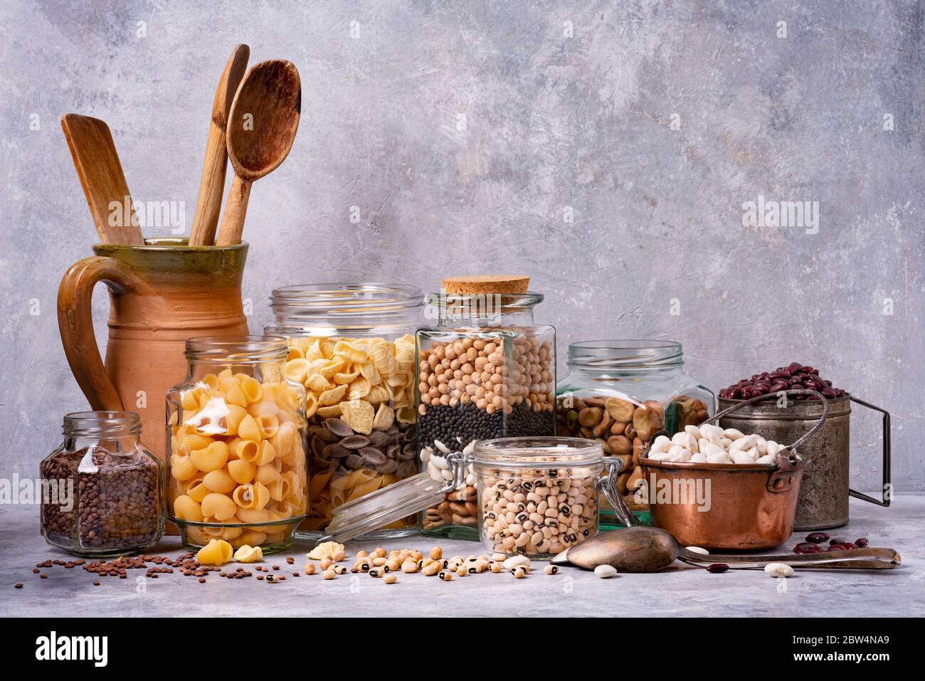 variety of dried legumes and Italian pasta in glass and metal jars. gray background texture. still life Stock Photo