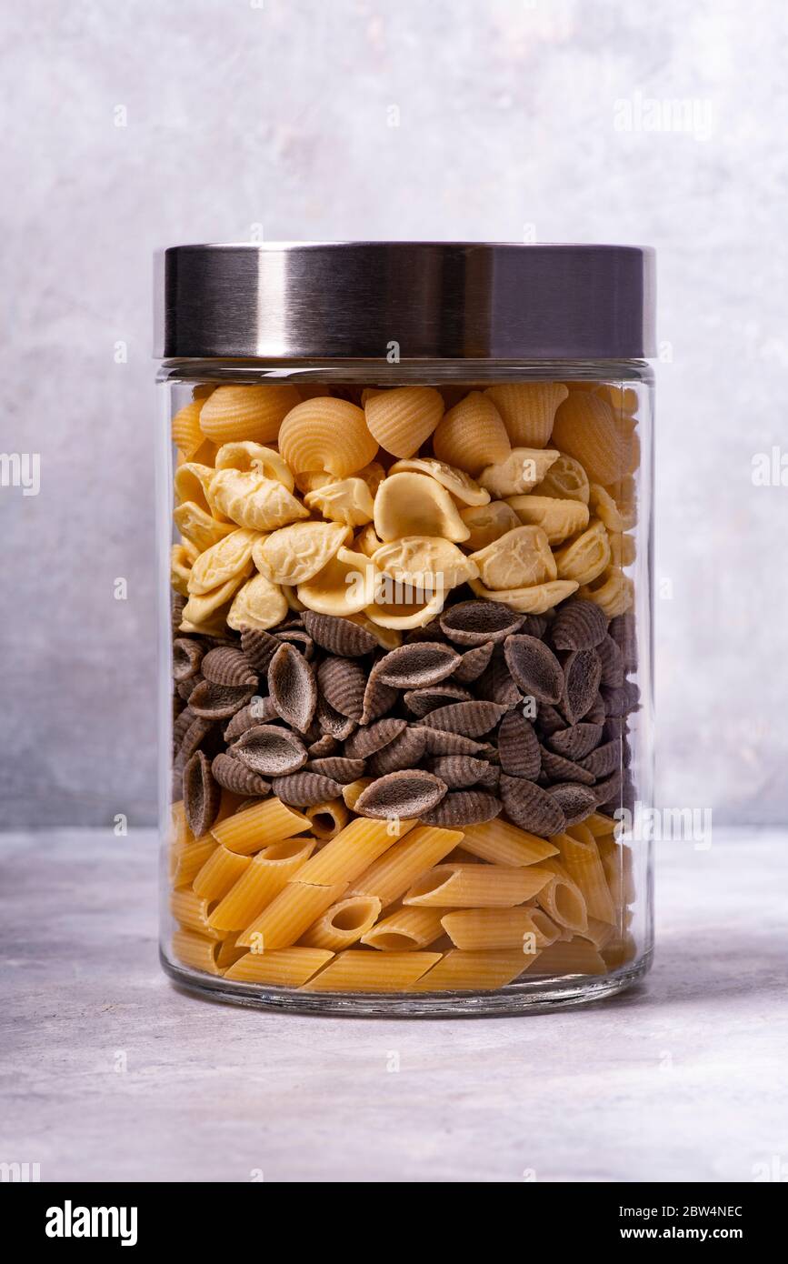 on a gray textured background, variety of Italian pasta in glass jar in the foreground. Mediterranean diet Stock Photo