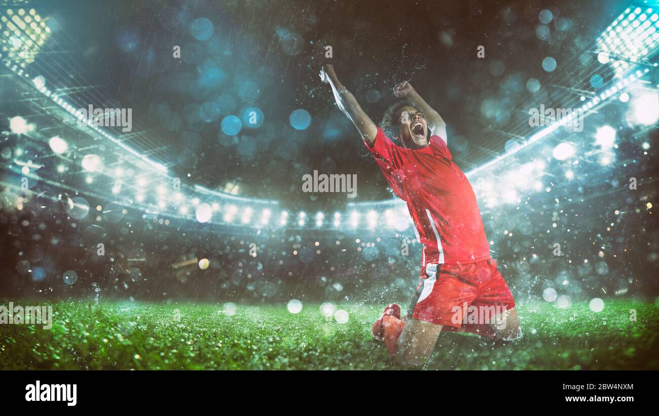 Soccer striker in red uniform rejoices for the victory at the stadium Stock Photo