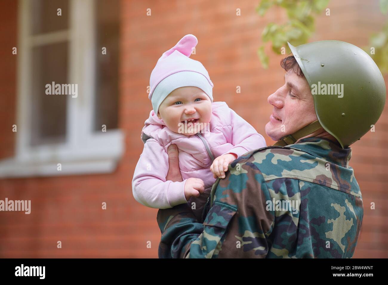 Military man in a helmet with a smiling little baby in his arms Stock Photo