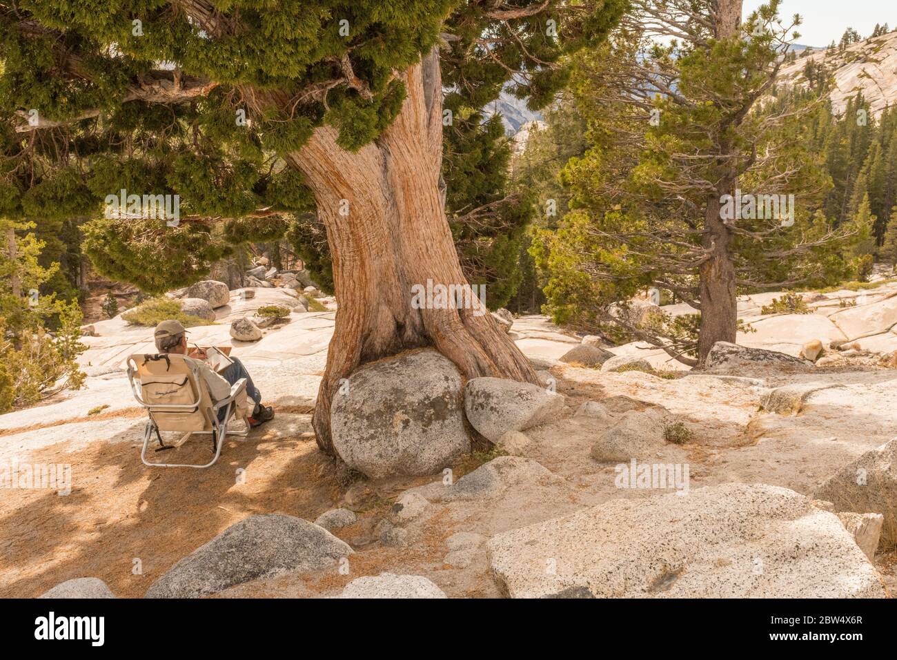 A man sitting in a folding chair takes notes in a notebook at Olmsted Point in Yosemite National Park Stock Photo