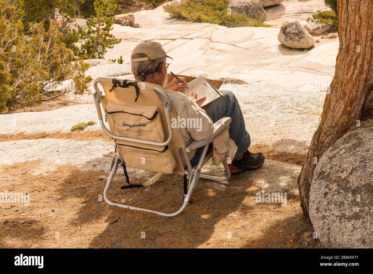 A man sitting in a folding chair takes notes in a notebook at Olmsted Point in Yosemite National Park Stock Photo