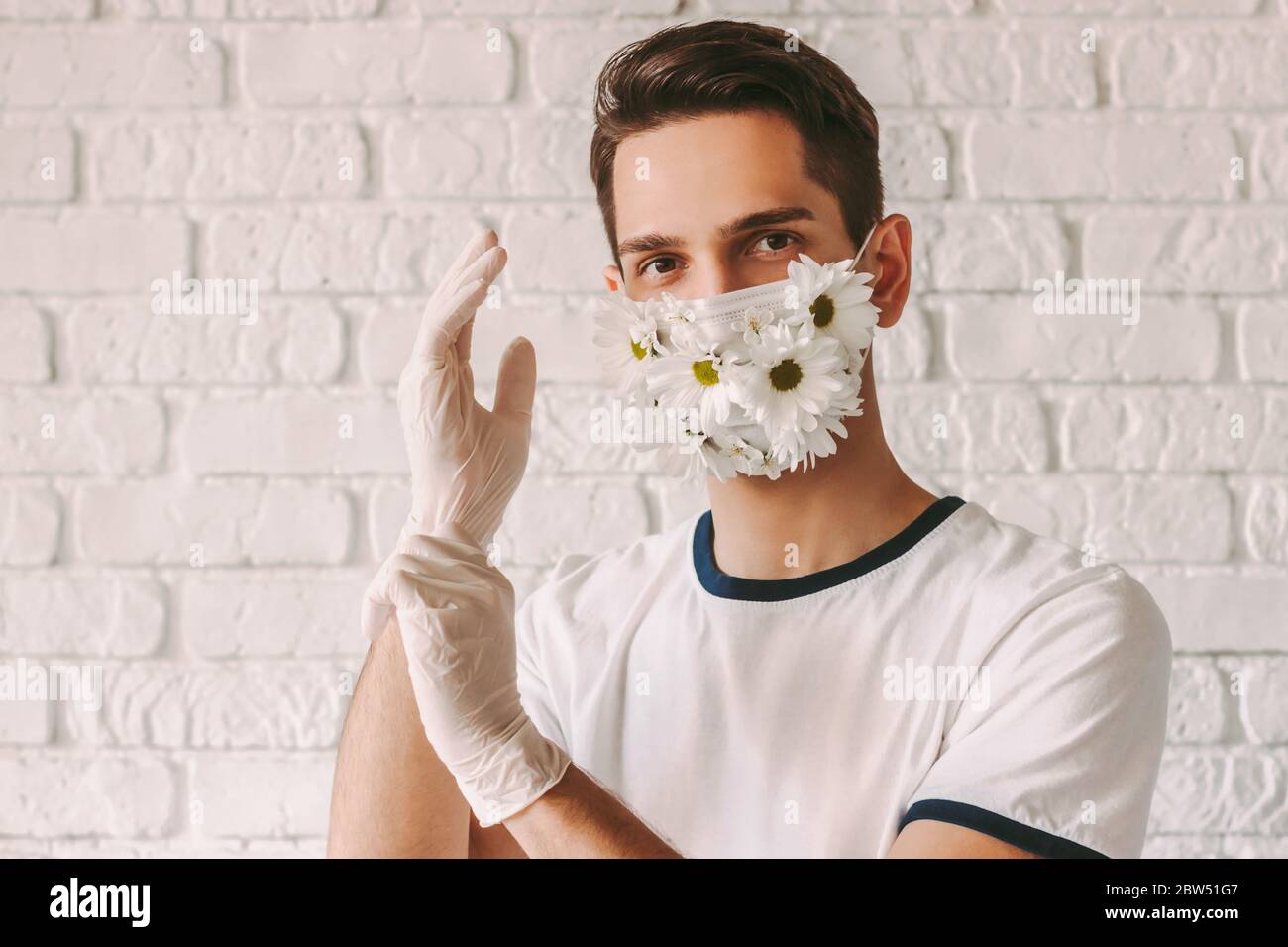Portrait of happy male doctor in daisy flower medical face mask put on latex protective gloves. Young man in summer protective face mask put on steril Stock Photo
