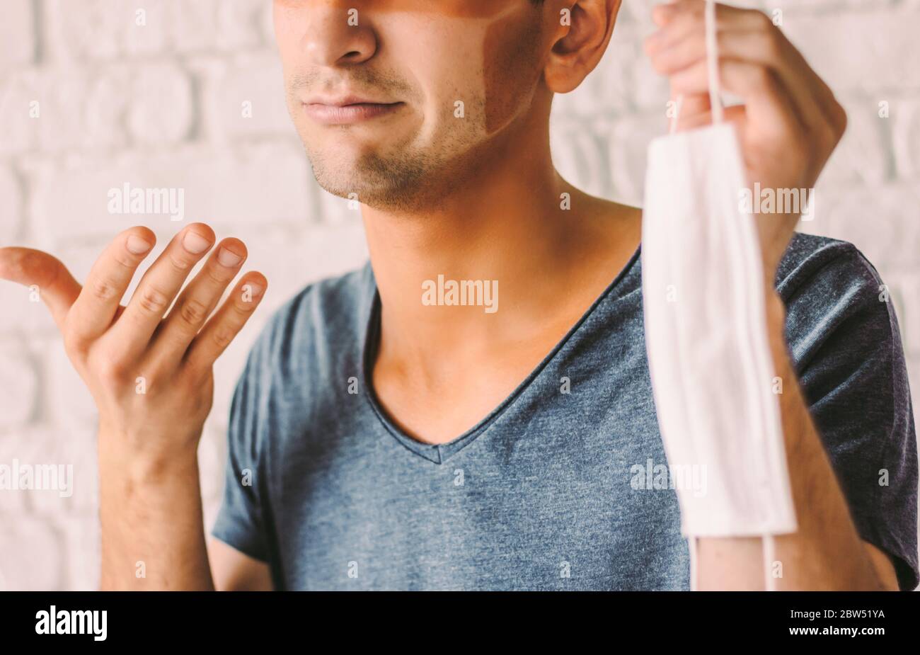 Portrait of young man patient with funny sun tanned lines on face after wearing medical face mask. Confused hipster man with sunburn tan face skin hol Stock Photo