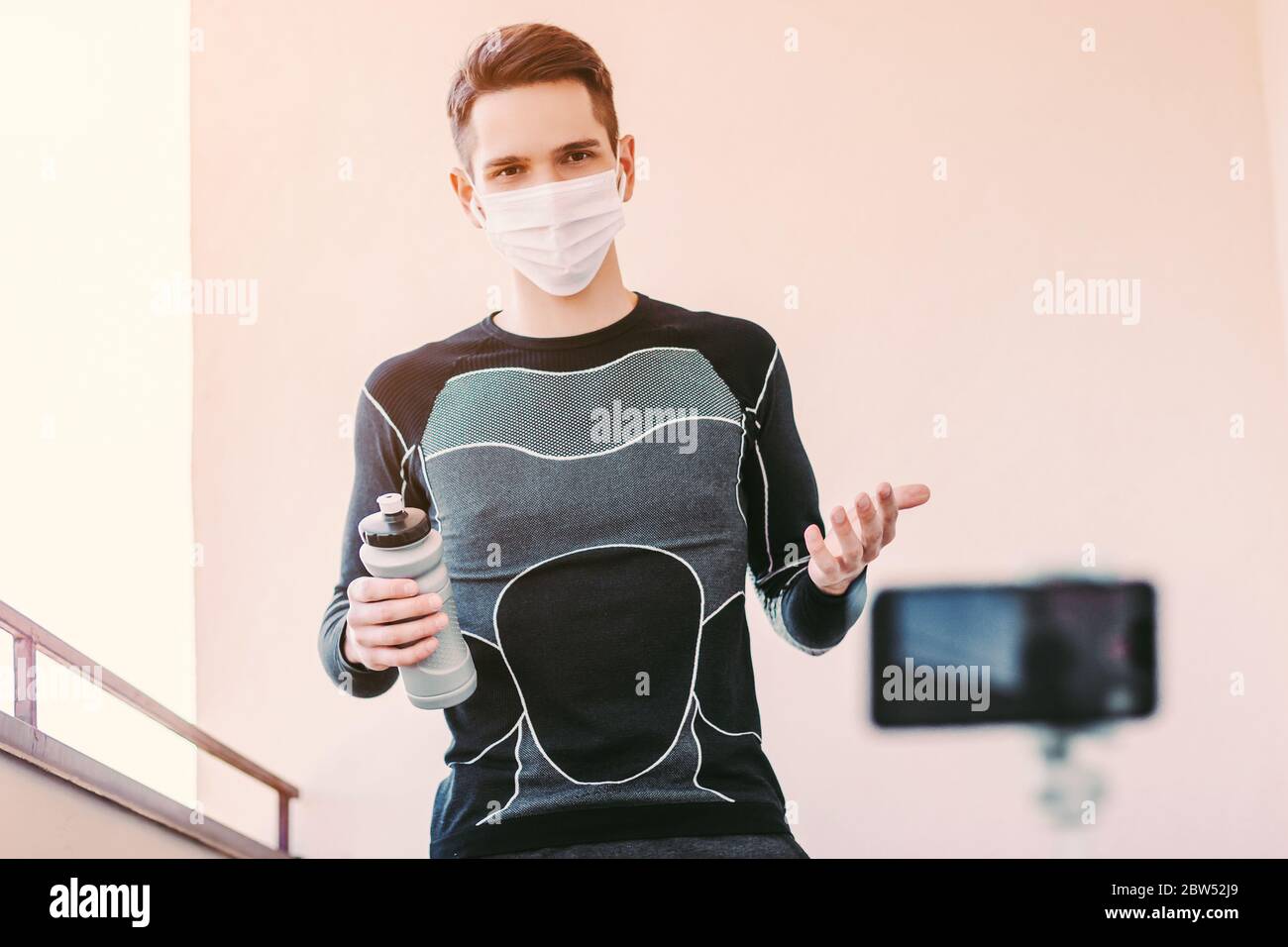 Young man fitness coach in medical face mask training against phone camera.  Confident sports man in protective mask record video tutorial for fitness  Stock Photo - Alamy