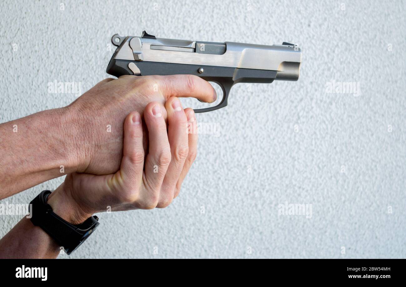 2 Caucasian male hands holding and aiming a semi-automatic pistol against a solid background with copy space Stock Photo