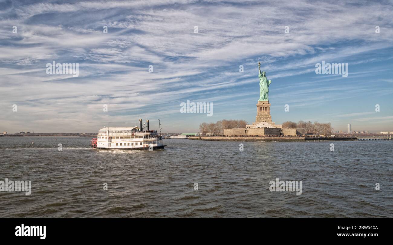 The Statue of Liberty in New York City USA daylight view with clouds in sky and ferry in the water Stock Photo