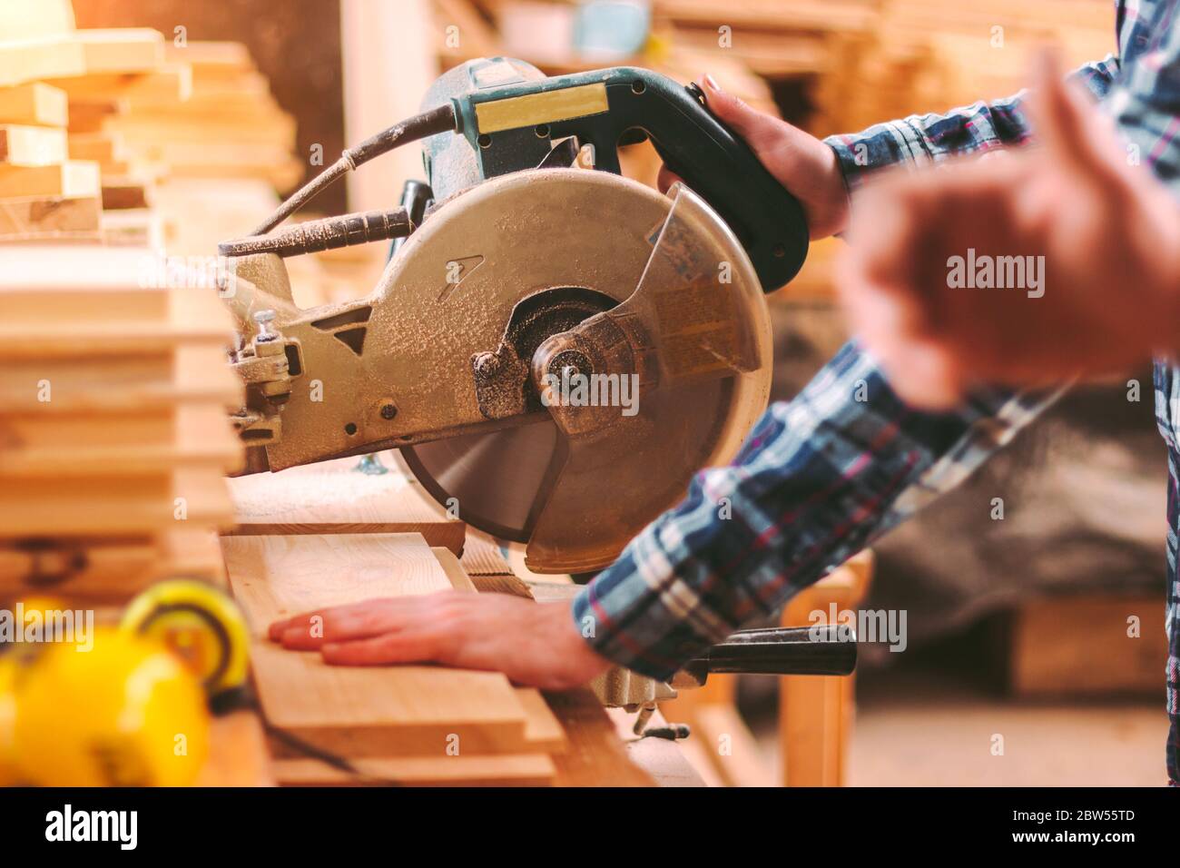 Closeup of professional cabinet makers working with electric circular saw at woodworking workshop. Skilled carpenter cutting wooden board with circula Stock Photo