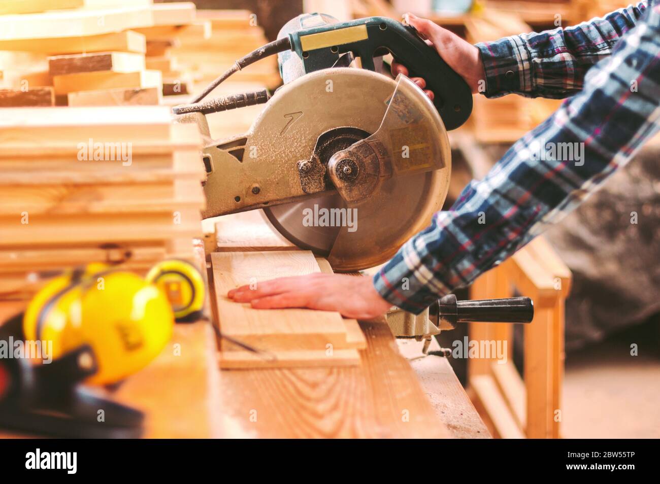 Closeup skilled maker cutting wood board with electric circular