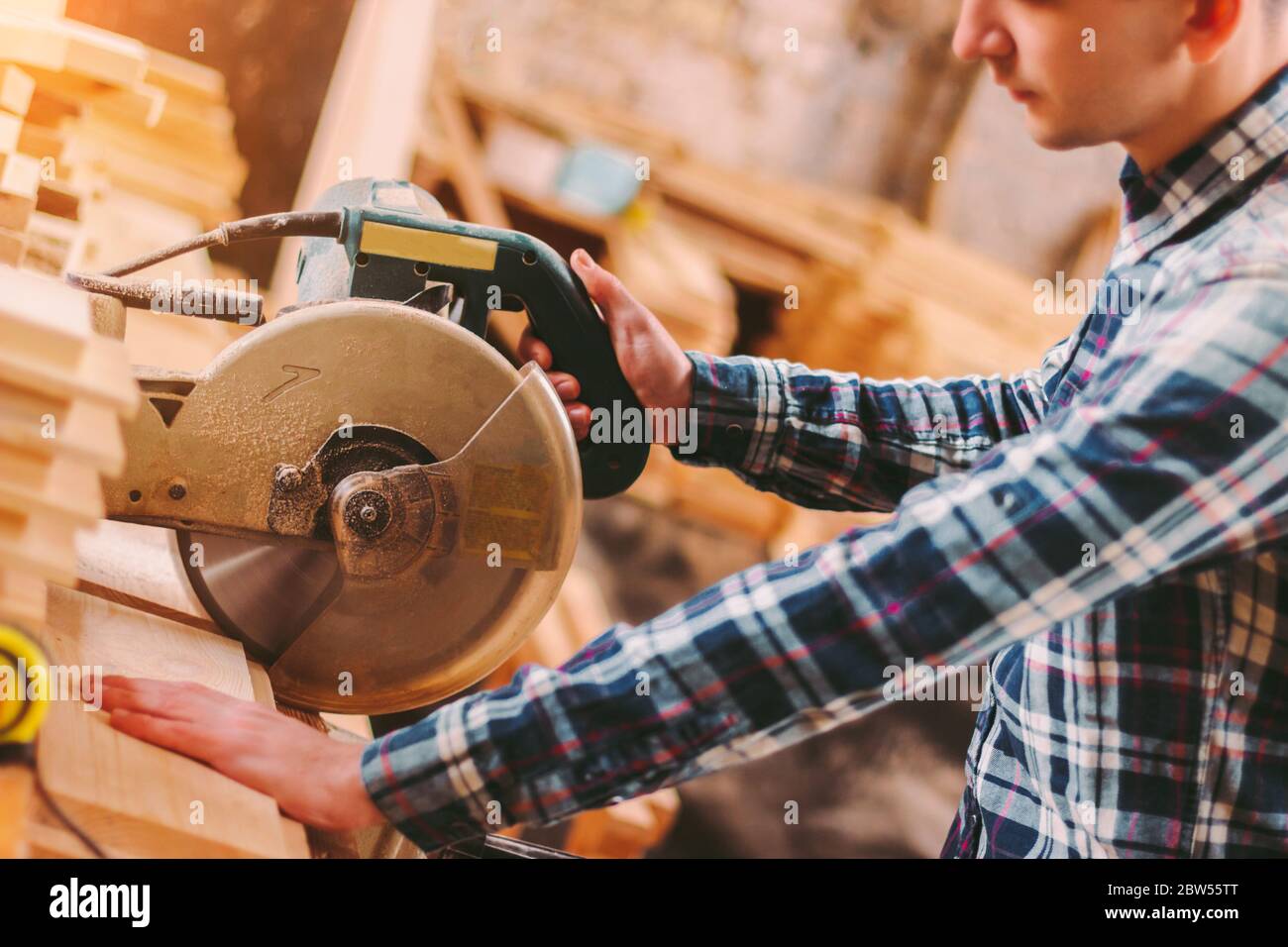 Closeup professional carpenter hold electric circular saw at sawmill