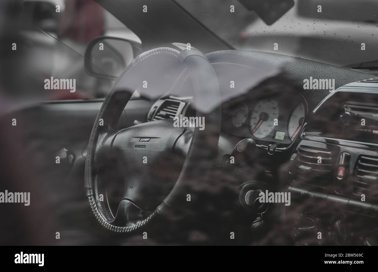 Black and white clean interior seen through glass of an older version of Fiat Bravo. White dashboard, wrapped steering wheel Stock Photo
