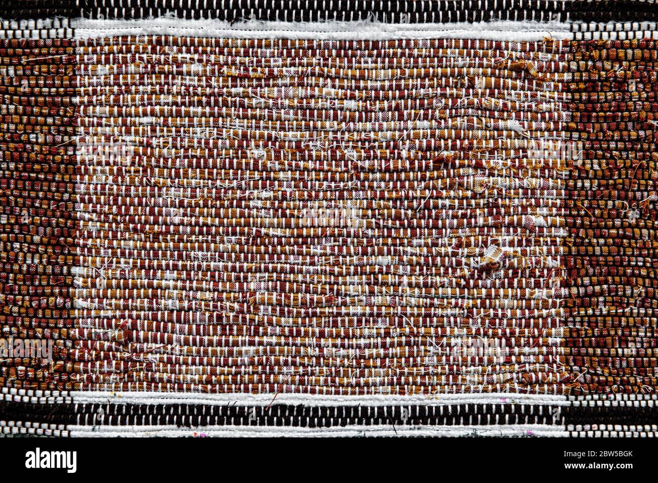 Colorful woven rug made of cotton thread. Handmade fabric fragment of brown color. Stock Photo