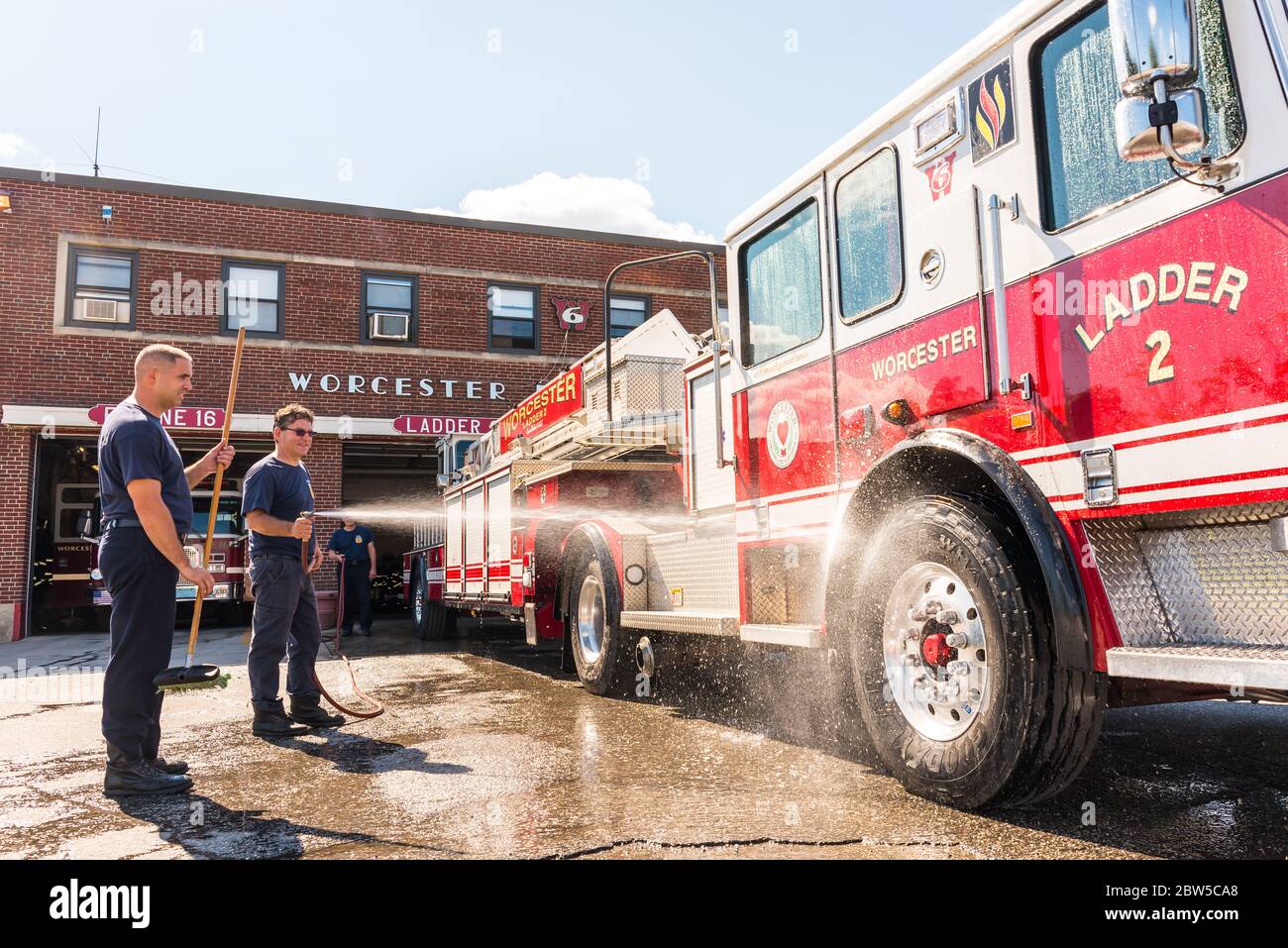 One firefighter cleaning a fire truck with water from a hose as another ...