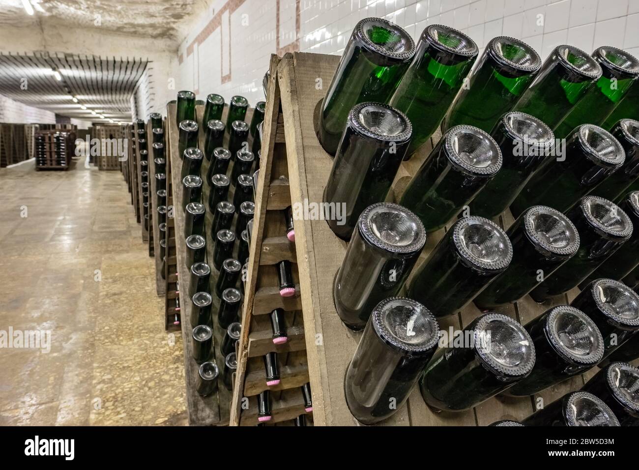 Sparkling wine bottles stacked up in old wine cellar close-up background. Stock Photo