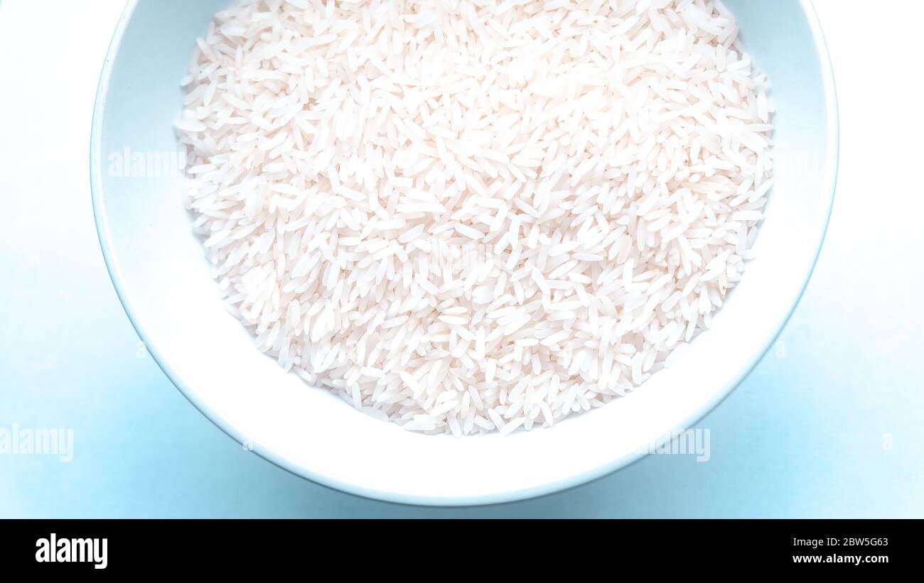 An overhead shot of a bowl of uncooked white rice with a bluish background Stock Photo