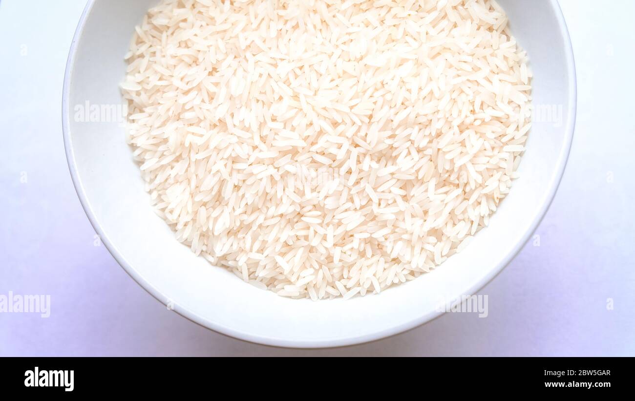 An overhead shot of a bowl of uncooked white rice with a purple background hue Stock Photo