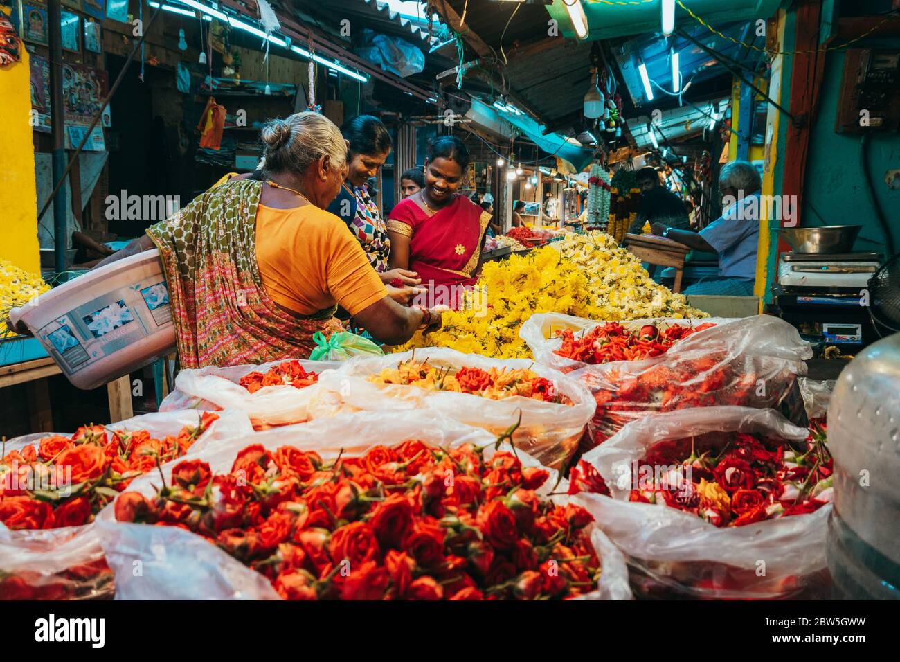 Three Indian women inspect flower petals for sale at a market in
