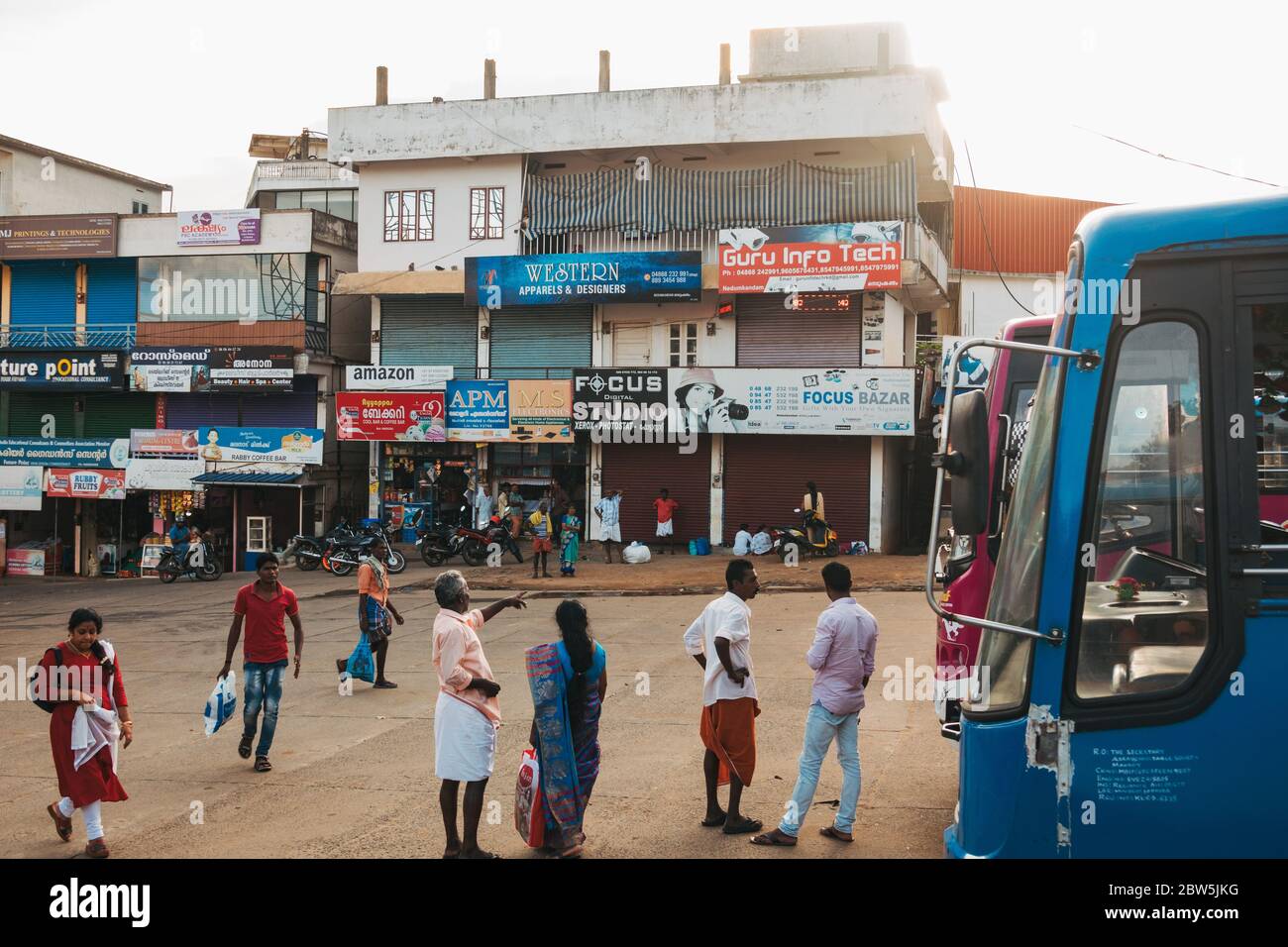 People standing on the forecourt of a rural bus station in Kerala, India Stock Photo