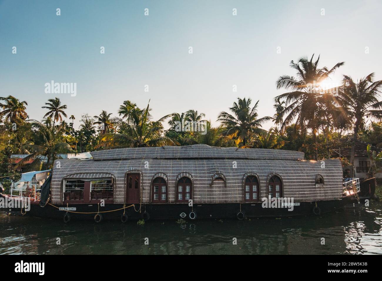 A houseboat cruises down a canal in the Kerala backwaters in the evening sun Stock Photo