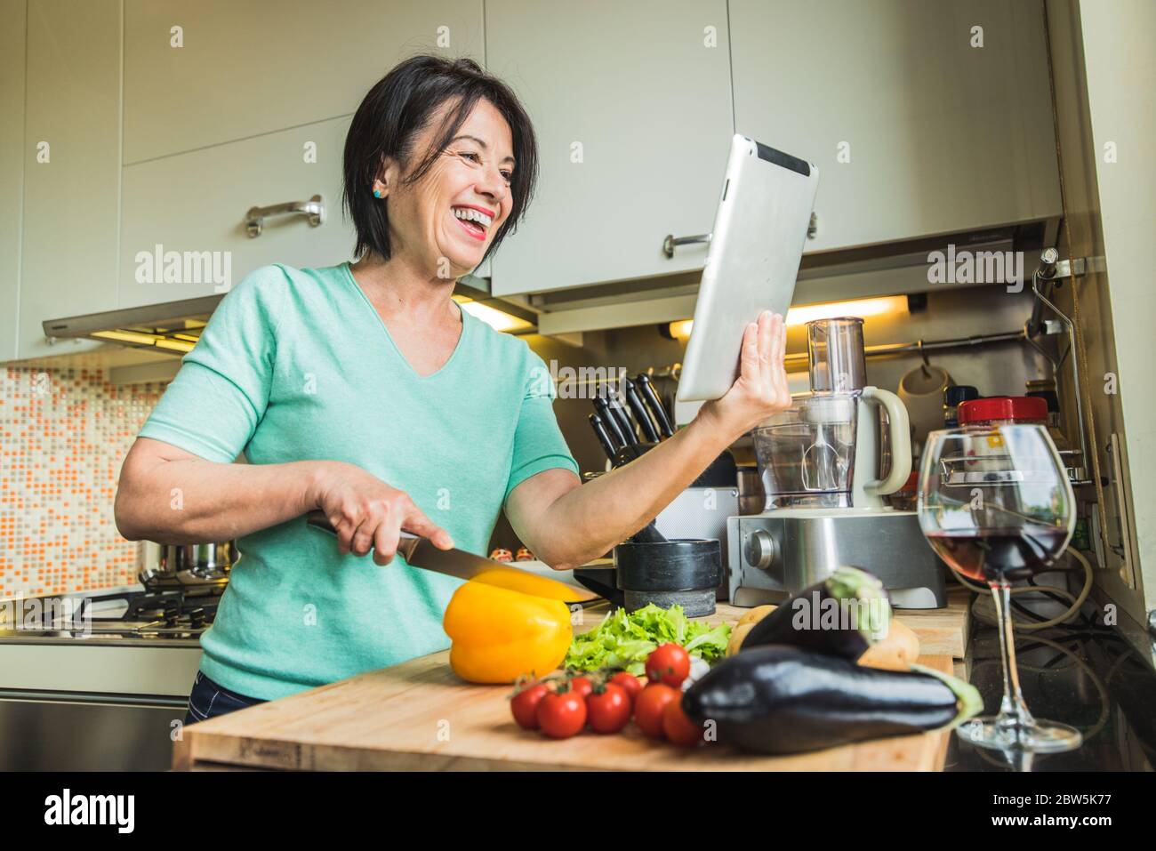 Senior woman cooking at home using digital tablet Stock Photo