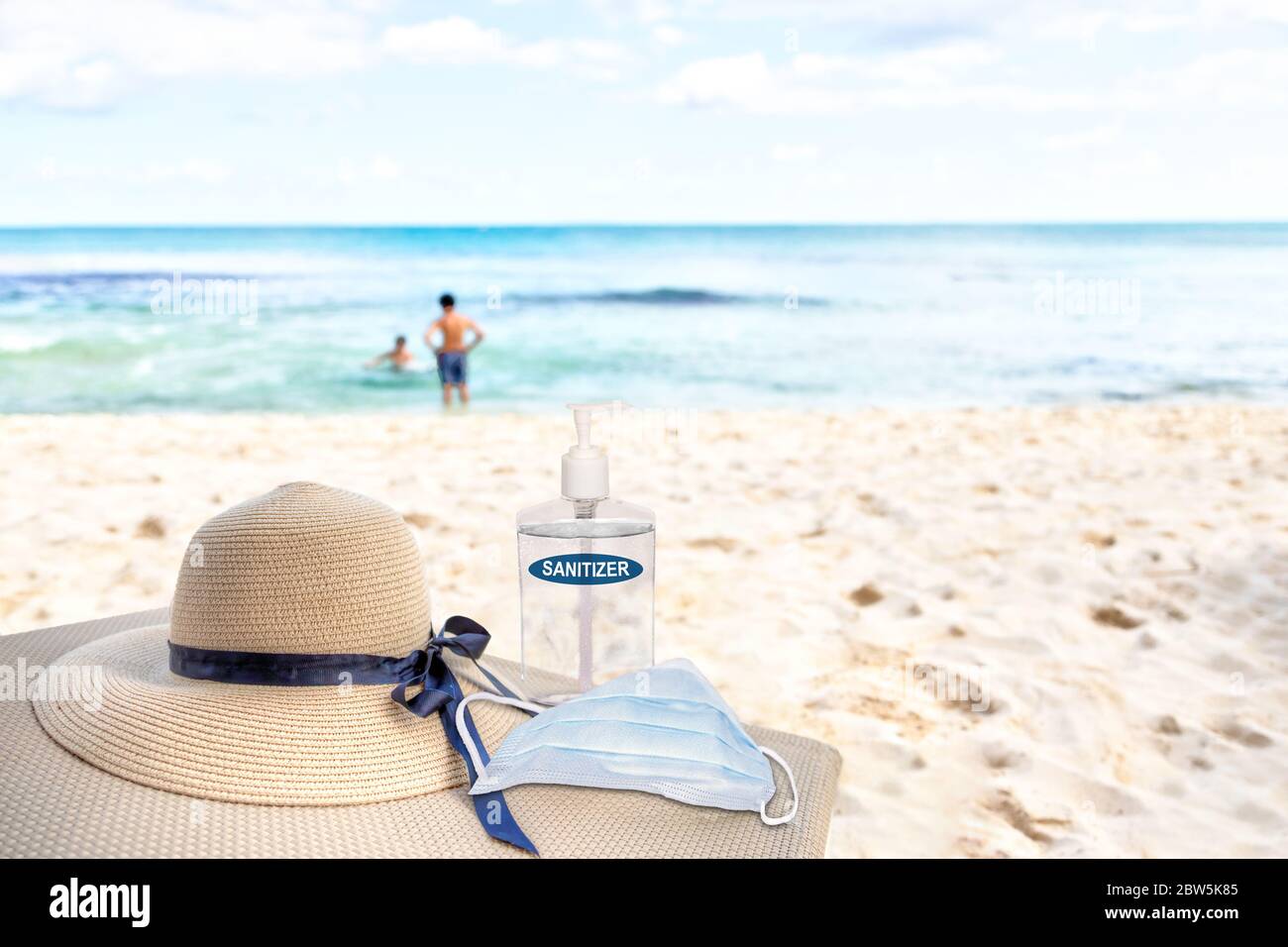 Vacationing in the New Normal after COVID-19 coronavirus pandemic. Tourism concept showing lounge chair on sandy beach with beach hat, hand sanitizer, Stock Photo