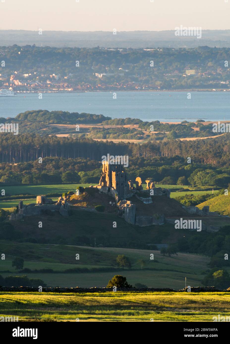 Corfe Castle, Dorset, UK.  29th May 2020.  UK Weather.  The view from Swyre Head of the ruins of Corfe Castle in Dorset illuminated by late afternoon sunshine at the end of a warm sunny day with clear skies with Poole Bay in the distance.  Picture Credit: Graham Hunt/Alamy Live News Stock Photo