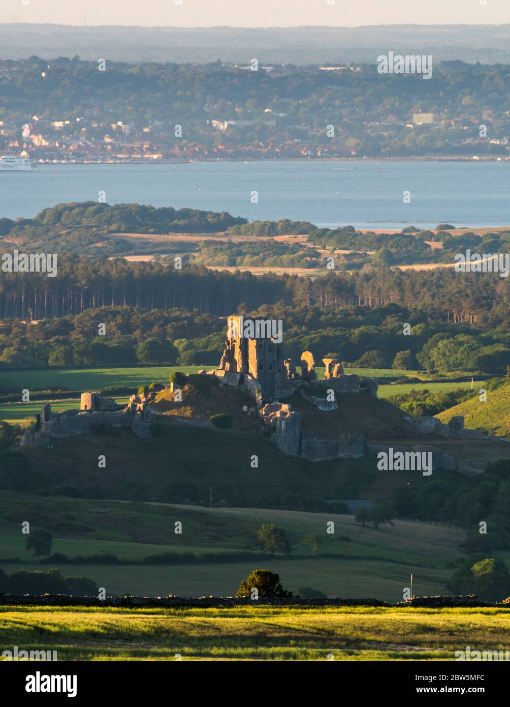 Corfe Castle, Dorset, UK.  29th May 2020.  UK Weather.  The view from Swyre Head of the ruins of Corfe Castle in Dorset illuminated by late afternoon sunshine at the end of a warm sunny day with clear skies with Poole Bay in the distance.  Picture Credit: Graham Hunt/Alamy Live News Stock Photo