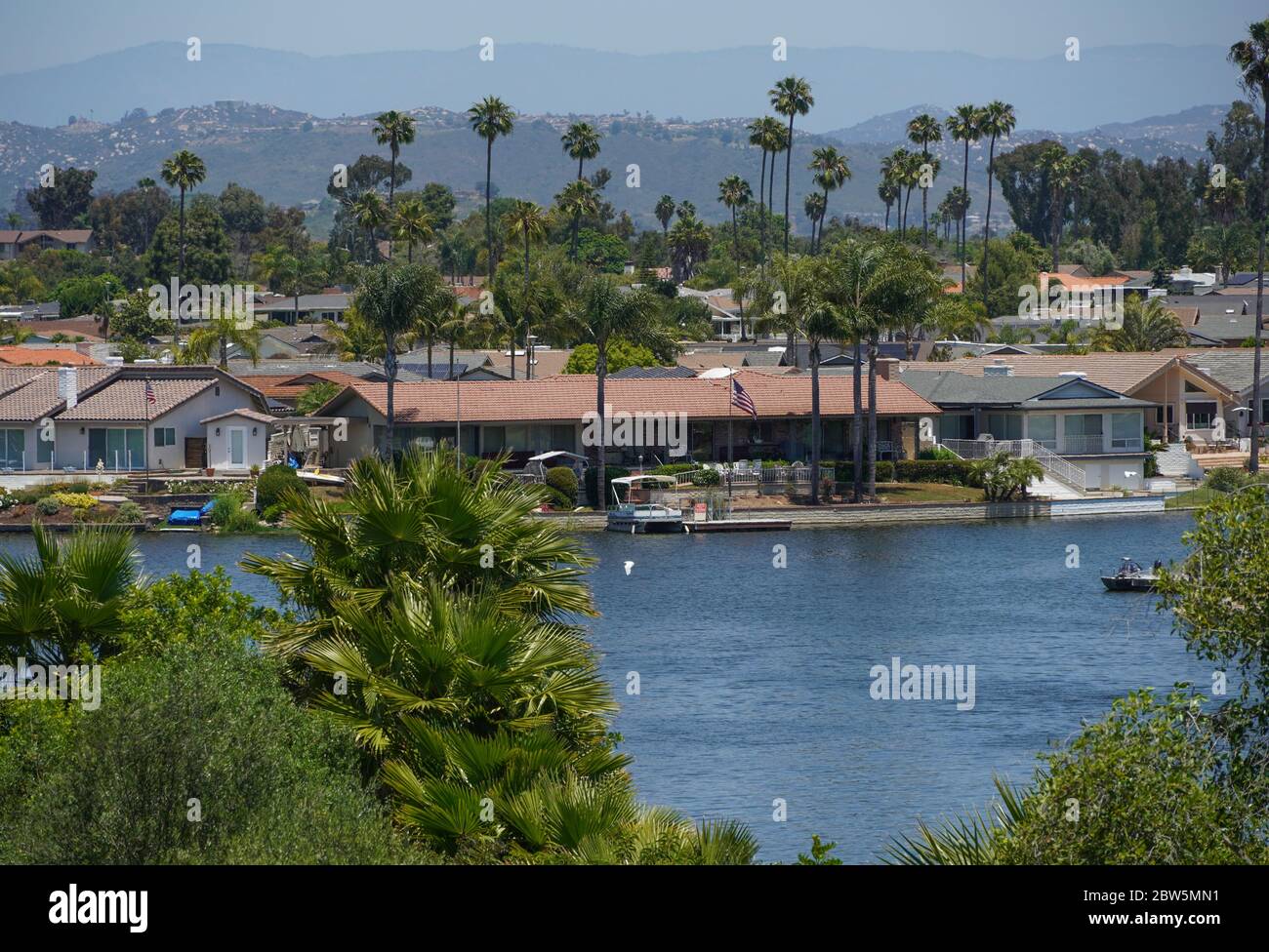 View across Lake San Marcos in San Diego County, California to shoreline residences and distant mountains. Pontoon boat, dock, palm trees, sunny. Stock Photo