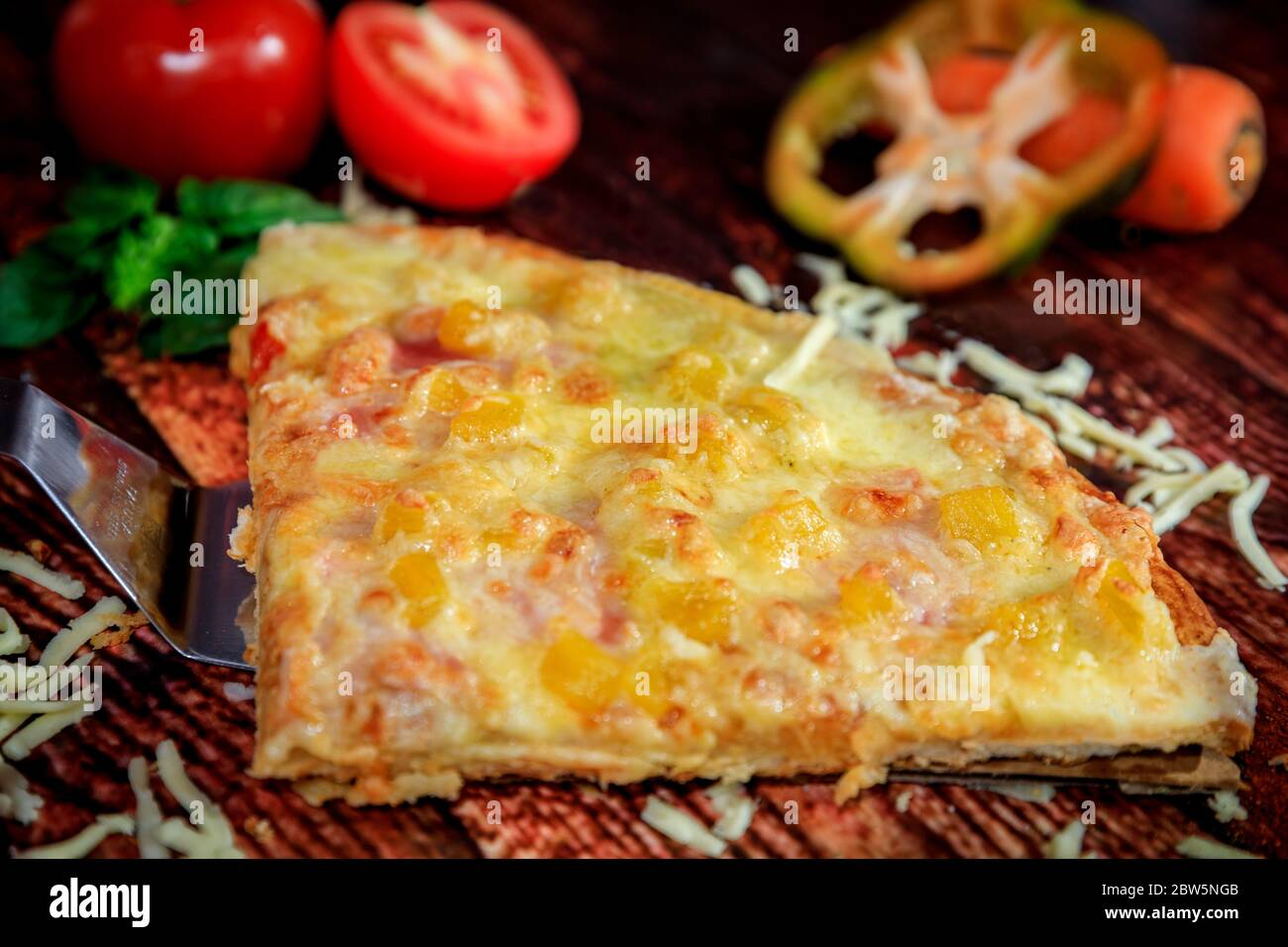 Front closeup of sweet Hawaiian pineapple pizza slice on dark wood background with fresh