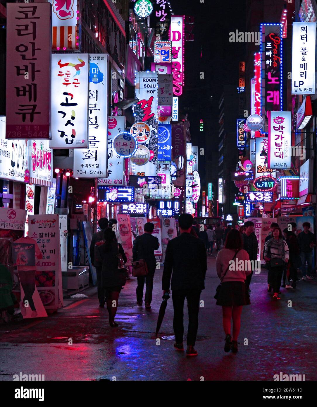 A rainy night walking down one of the shopping streets with neon shop signs of Myeong dong, Seoul, South Korea Stock Photo