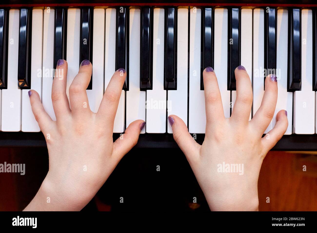 White Child's Hands Playing Piano Keyboard Viewed from Above Stock Photo