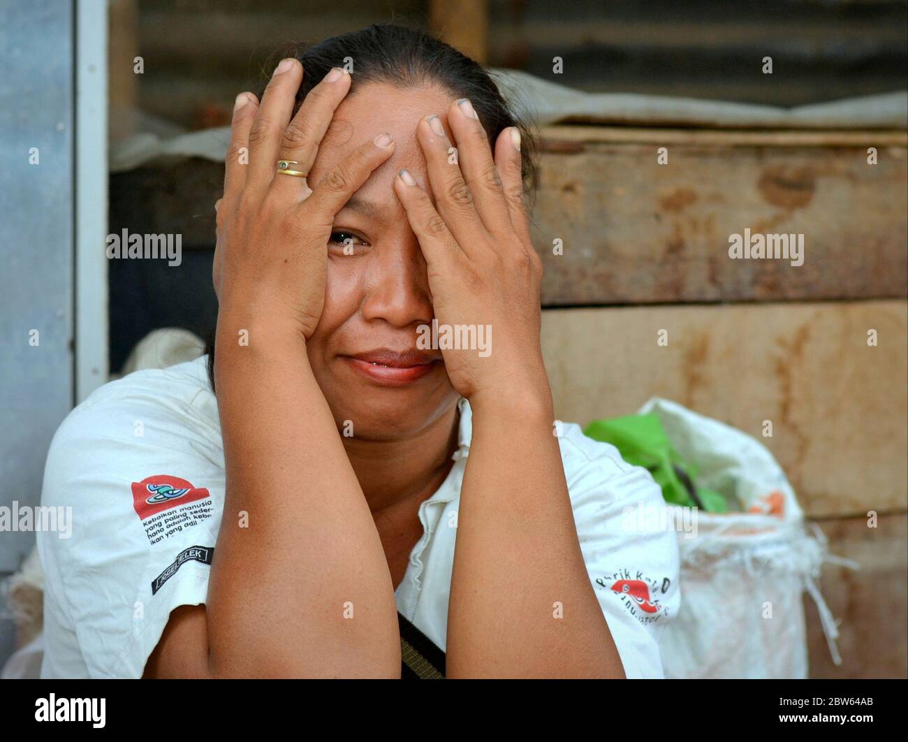Flirting mature Indonesian Javanese woman pretends to cover her eyes with both hands and mocks the photographer. Stock Photo